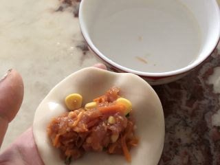 8、红萝卜玉米肉饺子,准备一碗水,拿一张饺子皮,加入适量的肉馅,然后用手指沾一下碗里的水,把整张饺子皮边缘涂抹一遍