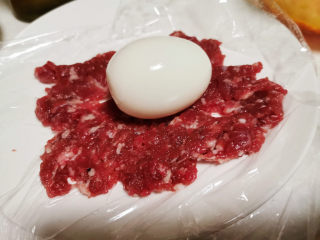 4、苏格兰炸鸡蛋-鸡蛋的花式吃法,盘子上铺一张保鲜膜，肉馅在保鲜膜上摊开压平，中间放一个鸡蛋。