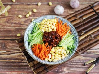 13、炸酱面,把面捞出放入面碗中,放上2~3勺炸酱,接着继续放上黄豆、黄瓜丝和胡萝卜丝。