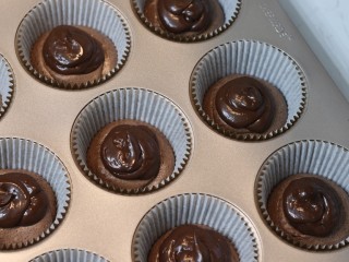 14、巧克力熔岩杯子蛋糕,将甘纳许装入裱花袋后挤在蛋糕糊中间（甘纳许挤多少没有要求，喜欢满满巧克力的可以多挤些。不过最好确保甘纳许不会挤到底部面糊边缘。甘纳许要和面糊边缘有一些空间）