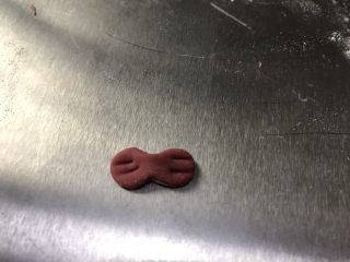 12、猪猪馒头,取1g左右红色面团揉成椭圆形压扁，中间按压一下，两边用牙签压出痕迹，做成蝴蝶结