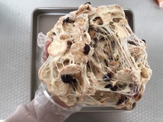 9、网红草莓雪花酥,将雪花酥料拿起来，用手反复柔和，拉丝，这样让棉花糖均匀的裹在坚果和饼干上，雪花酥就会更有嚼劲，而且也不会硬