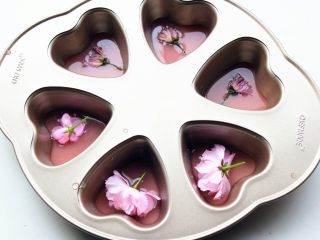 5、樱花草莓慕斯,把用来做镜面的那部分草莓吉利丁溶液，倒一半到学厨六连心形模内，再放上一朵樱花，然后放入冰箱冷藏40分钟，等凝固。我还用了三朵盐渍樱花，盐渍樱