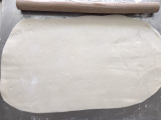 3、葱油花卷,台面上多撒些干粉防粘，用手先压扁面团，然后把擀面杖放在中间，往两头擀，用擀面杖擀成厚度约3到4毫米的长方形面片。