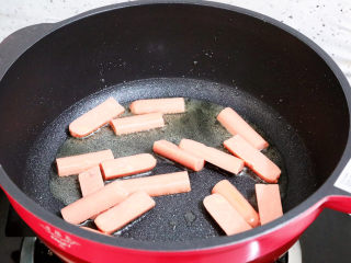 5、香辣孜然火腿肠炒年糕,锅中倒入适量的食用油烧热，放入火腿肠煎至表面金黄色