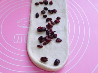 8、波兰种蔓越莓吐司面包,取一块面团，用擀面杖擀开，将气泡拍破，再放入蔓越莓干，将擀好的长舌状两边向中间对折，用擀面杖轻轻擀长，由上而下卷起。