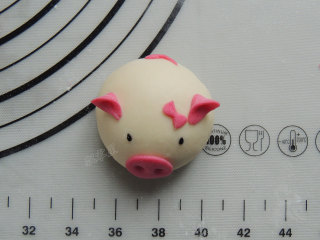 15、卡通小猪馒头,将做好的猪鼻子、猪耳朵、猪尾巴和蝴蝶节底部蘸一点清水,摆放到白色面团的对应位置。黑芝麻蘸水沾到面团上,当做眼睛。