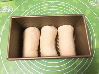 8、快速早餐吐司片-椰蓉味,将剂子擀成椭圆形，顺势卷起来，依次放入吐司盒。
