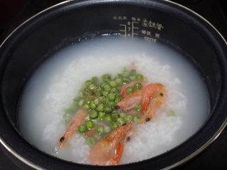 9、#电饭煲# 蔬菜海鲜粥,打开电饭煲，放入刚煸好豌豆大虾、用饭勺搅拌均匀加盖继续