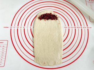 8、牛奶炼乳蔓越莓软欧,取一份松弛好的面团，用擀面杖擀成长方形，取8克蔓越莓碎放入面片顶端，轻轻压一下。