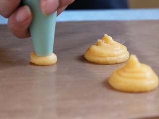 12、酥皮泡芙,将面糊装入裱花袋,这里加了1cm口径的裱花嘴挤,面糊的大小控制在3-4cm。挤每个面糊时,裱花口垂直于桌桌面,收尾时在中心点扭一圈上提。