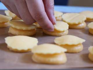 13、酥皮泡芙,快速将冰箱取出的酥皮盖在挤好的泡芙糊上。泡芙糊上的尖尖顺手轻轻压平些。放入预热200度的烤箱中层35分钟,中途不能打开烤箱,泡芙会塌。
