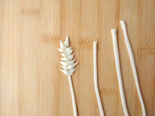 14、原味麦香小面包,制作麦穗：将一块儿面团擀成薄片，切细条，另用手将一小块面团搓成一头尖，一头圆的样子，按照对生的次序黏在上面。