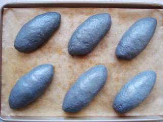 11、竹炭软欧包,收口向下放，整理成橄榄形。依次做好，放入烤盘中。盖上保鲜膜开始第二次发酵。（约40分钟）