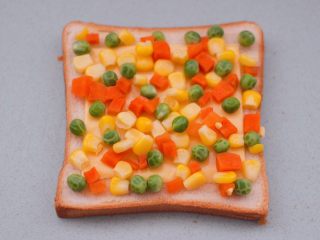 7、田园时蔬吐司披萨,把焯过水的玉米粒和豌豆，胡萝卜丁均匀地铺上奶酪片上。