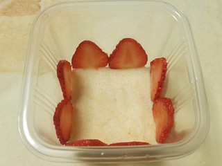 15、送你一朵小红花,开始组装。先在包装盒底部装一片裁好的蛋糕胚，周围摆上草莓片，紧贴着摆