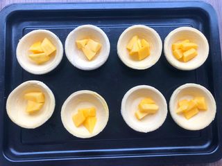 4、芒果酥,把蛋挞皮一个一个放入盘子里，把芒果块放入蛋挞皮里。