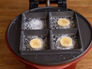 8、湿润蓬松【香蕉椰蓉蛋糕】好吃的不得了,小红锅装上布朗尼烤盘最高温预热完成后，每个模具中撒入椰蓉，放入香蕉片，舀入约45g面糊（挖球勺1平勺）。