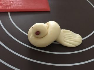 9、小鸟馒头,再像平常打结一样，给面条打个结，稍微整形一下！在头部那里捏出一个小尖嘴巴！用红豆代替小鸟的眼睛！尾巴部分用手掌压扁，用刀背或者用刮板压出纹理！