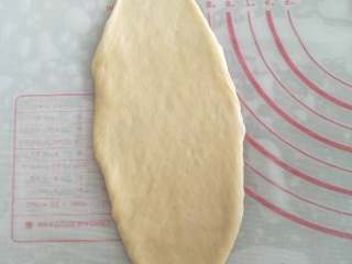 5、蜂蜜脆底小面包, 取一个圆面团,用排气擀面棍将面团擀成23CM长的椭圆形。右手用刮板将面团铲起,左手将面团翻面。