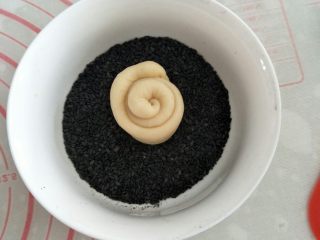 9、蜂蜜脆底小面包,取一小碗盛装黑芝麻芝麻,将面团底部粘上黑芝麻