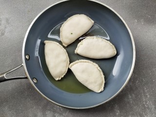 9、韭菜盒子,热锅倒少许的油润锅，将韭菜盒子放入，小火煎至一分钟左右，底部微黄后翻面