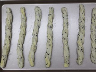 10、黑芝麻椰蓉面包棒,取一份小面团，两手向相反的方向搓成螺纹条，放在垫好油纸的烤盘上稍微按压下，不然最后发酵后和烤时卷会散开了就不好看了