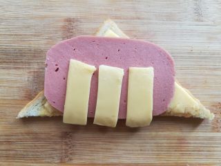 12、百变大眼怪三明治,先把吐司面上的一块取下，放上火腿肠片和芝士条