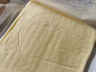 11、榴莲卷【啖啖肉、软绵绵】,蛋糕焗好出炉，，移架子上散热几分钟后，在上面铺层新的油纸，把蛋糕反转，撕掉焗蛋糕的那层油纸，再反转过来放在油纸上。