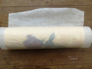 26、彩绘玫瑰蛋糕卷,利用擀面杖反卷底部油纸的方式慢慢推送蛋糕片，使蛋糕片自然往前卷起，卷好后油纸包起整条蛋糕卷，底边朝下放置，送入冰箱冷藏1小时定型