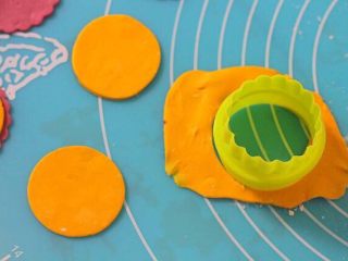 11、［鹿小鹿］翻糖卡通纸杯蛋糕,取小号的圆形饼干模，在黄色的翻糖片上切出圆形，用清水粘贴在淡紫色的翻糖片上。