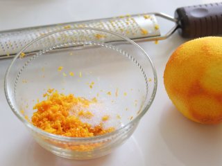 1、橙味甜甜圈蛋糕，在家就可复刻的经典美味,橙子一个，用小苏打洗净，用盐再搓一搓洗干净。用刨刀刨出橙皮碎，用3-5克糖腌制一下。