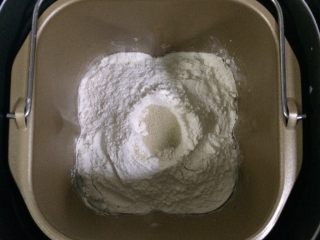 1、培根口蘑田园披萨,除黄油以外的面包材料都放入面包机内（先液体后粉类的顺序），在面粉中间挖个洞，把酵母粉倒进去，启动和面程序。