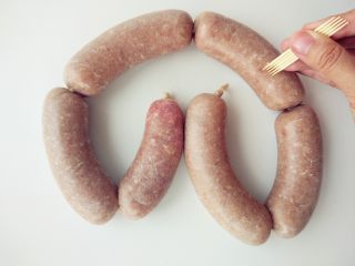 15、烧麦灌香肠土豆丝饼套餐,用香肠锥或牙签在表面扎一些孔，这样煮的时候不会涨破。捏住香肠两端，像摇绳一样，第一段超前转动两三圈，第二段向后转动两三圈，并且把肉馅稍往中间