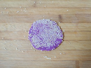 13、紫薯芝麻饼,放在案板上用擀面杖轻轻擀一下，让芝麻牢牢的粘在紫薯饼上，不易脱落。