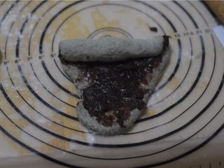 12、黑芝麻红豆土司,将剂子擀成牛舌状,抹上红豆泥,从上至下卷起来