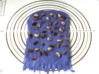 11、面包机版星空面包,取小的蓝面团，擀成宽度与面包桶内宽差不多的长方形，底部压薄，均匀布上开心果和葡萄干。