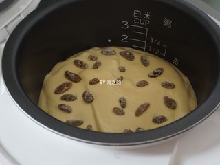 11、电饭锅戚风蛋糕,蛋糕糊倒入电饭锅内胆，在桌面上震两下，震出气泡，然后在上面铺上剩余的葡萄干装饰