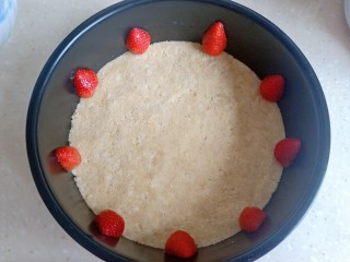 5、酸奶慕斯蛋糕,将搅拌好的饼干碎倒入蛋糕模具中，模具最好是可以脱膜的。倒入后把饼干碎用东西压平压紧，加上自己喜欢的水果盖上保鲜膜放入冰箱冷藏。