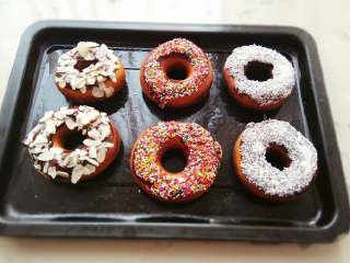 6、甜甜圈,趁热将甜甜圈裹一层糖粉即可食用。也可以将巧克力放碗里加少许水隔热融化，将炸好的甜甜圈的一面裹一层巧克力酱，然后再蘸上准备好的糖针、椰蓉或杏仁片。