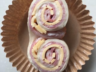 13、培根芝士卷,面团收口朝下，从中间切开但是不切断，翻开呈两个圆柱体，放入圆形纸膜中。