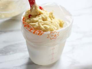 5、黄油曲奇,将花嘴放入裱花袋口,将裱花袋如图放入一个量杯,然后将曲奇面糊放入裱花袋中。