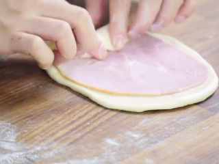 8、火腿芝士面包,面团擀成椭圆形，放入火腿片，卷起，捏紧收口处，