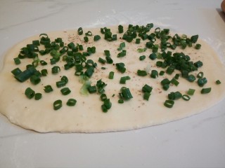 7、#咸味#快速发酵的花卷,将面团对半切开，撒少许干面粉，将面团擀成长方形的面饼，在面饼表面淋少许油，均匀刷开，撒少许细盐，椒盐，香葱，用手按压一下香葱，增加香葱的牢固度