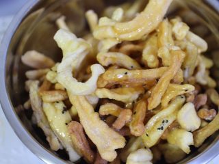 13、沙琪玛,将糖浆倒入到炸好的面条盆子里,然后在撒上适量的黑芝麻,用刮刀充分翻拌均匀,一定要让每个面条都裹上糖浆,面条盆子最好大一点,方便翻拌混合