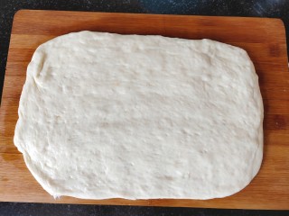 5、简单快手炸油条,发好的面团轻轻拍扁，擀成长薄饼状。