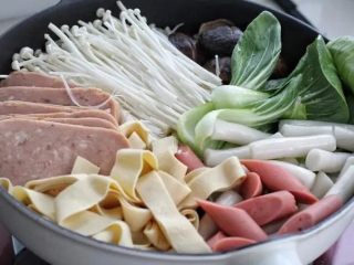 6、部队火锅,然后将午餐肉、金针菇、香菇、油菜、年糕、火腿肠、干豆腐依次摆放锅中。