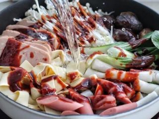 7、部队火锅,画圈淋入酱汁，再倒入清水盖上锅盖大火煮至沸腾。