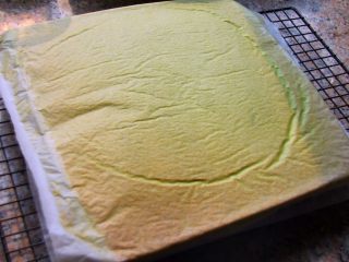 16、抹茶漩涡蛋糕,16．	烤好之后，将烤盘摔一下，震出里面的热气，然后倒扣在铺有油纸的晾网上，趁热揭掉油纸，上面虚盖一张油纸，晾凉。