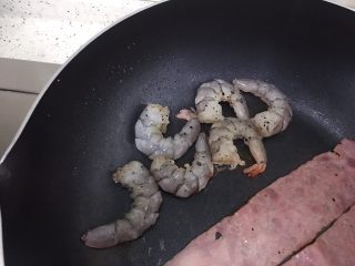 7、创意培根鲜虾鸡蛋三明治,step6:借着炒鸡蛋后锅中的底油煎培根和虾，依旧是小火，一定要勤翻面，培根本来就是熟的所以不用很久，虾也非常好熟。